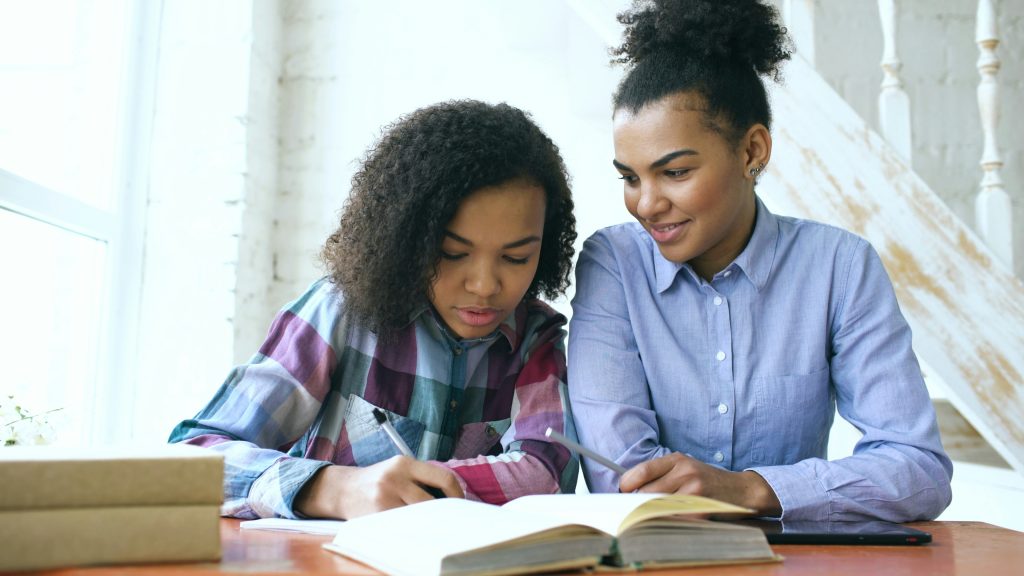 A tutor helping a student with math at a desk with open books